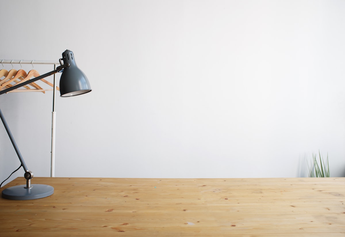 An adjustable-arm desk lamp on a wooden desk against a pale wall
